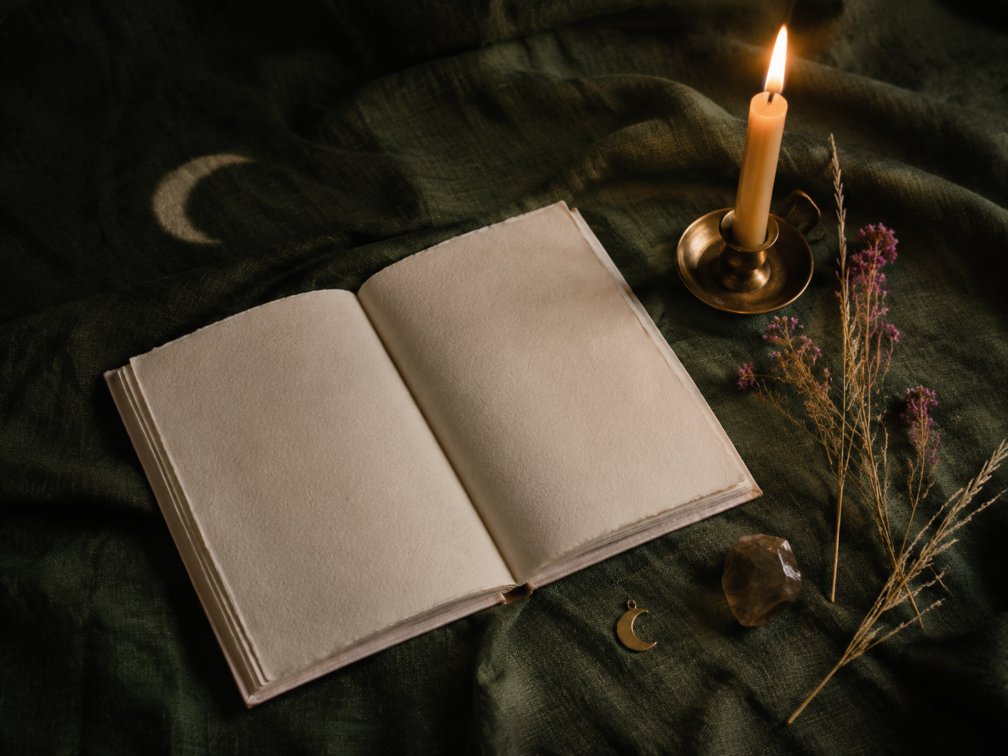 An open journal, candle and dried botanicals arranged on deep green linen